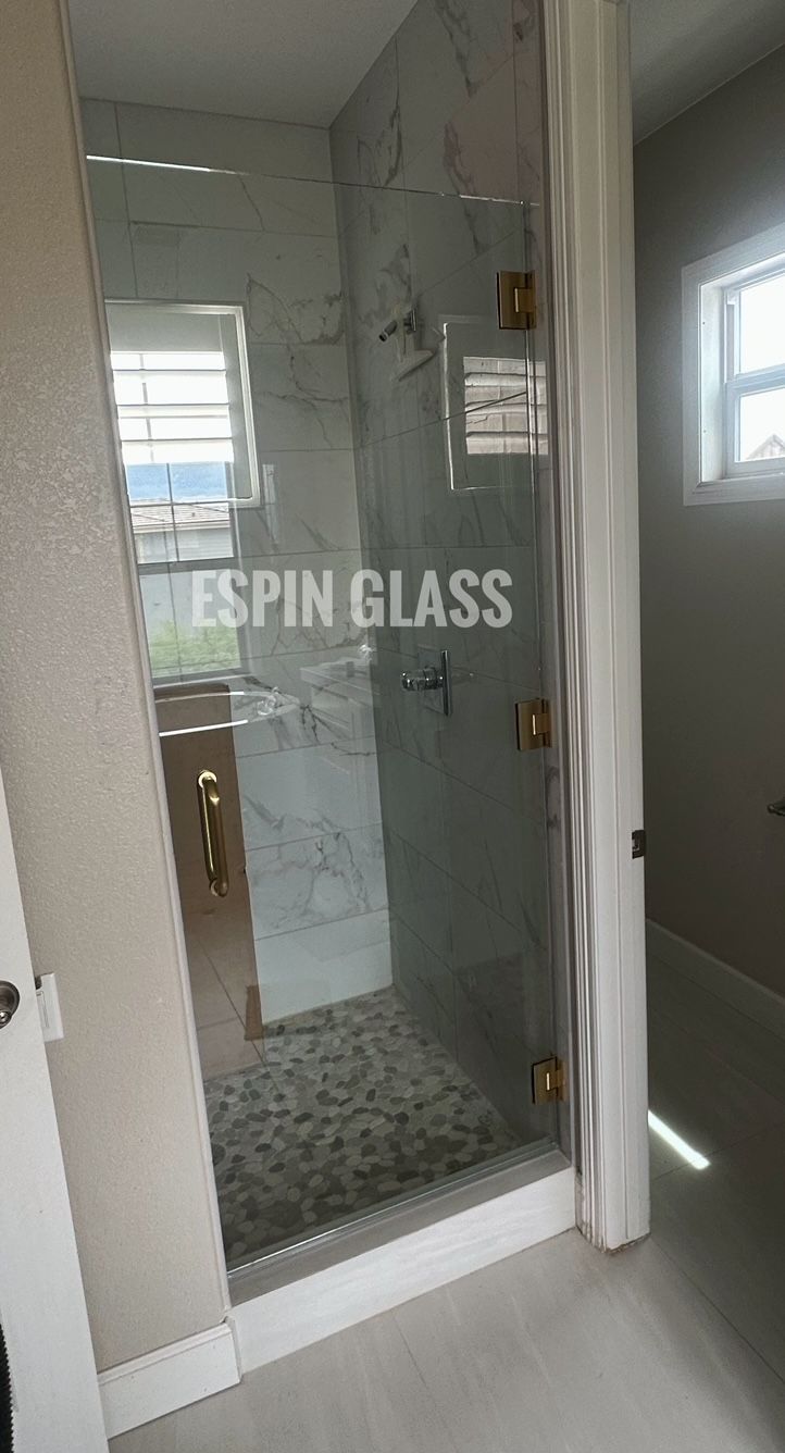 Glass shower enclosure with gold hardware; white tile, marble pattern, and light gray walls.