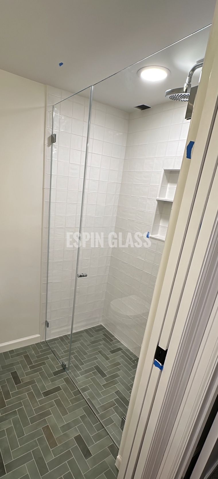 Glass shower enclosure in a bathroom with gray tiled floor and white walls.