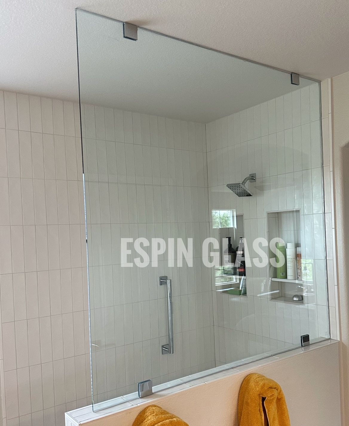 Frameless glass shower enclosure with a chrome handle, set against white tiled walls.