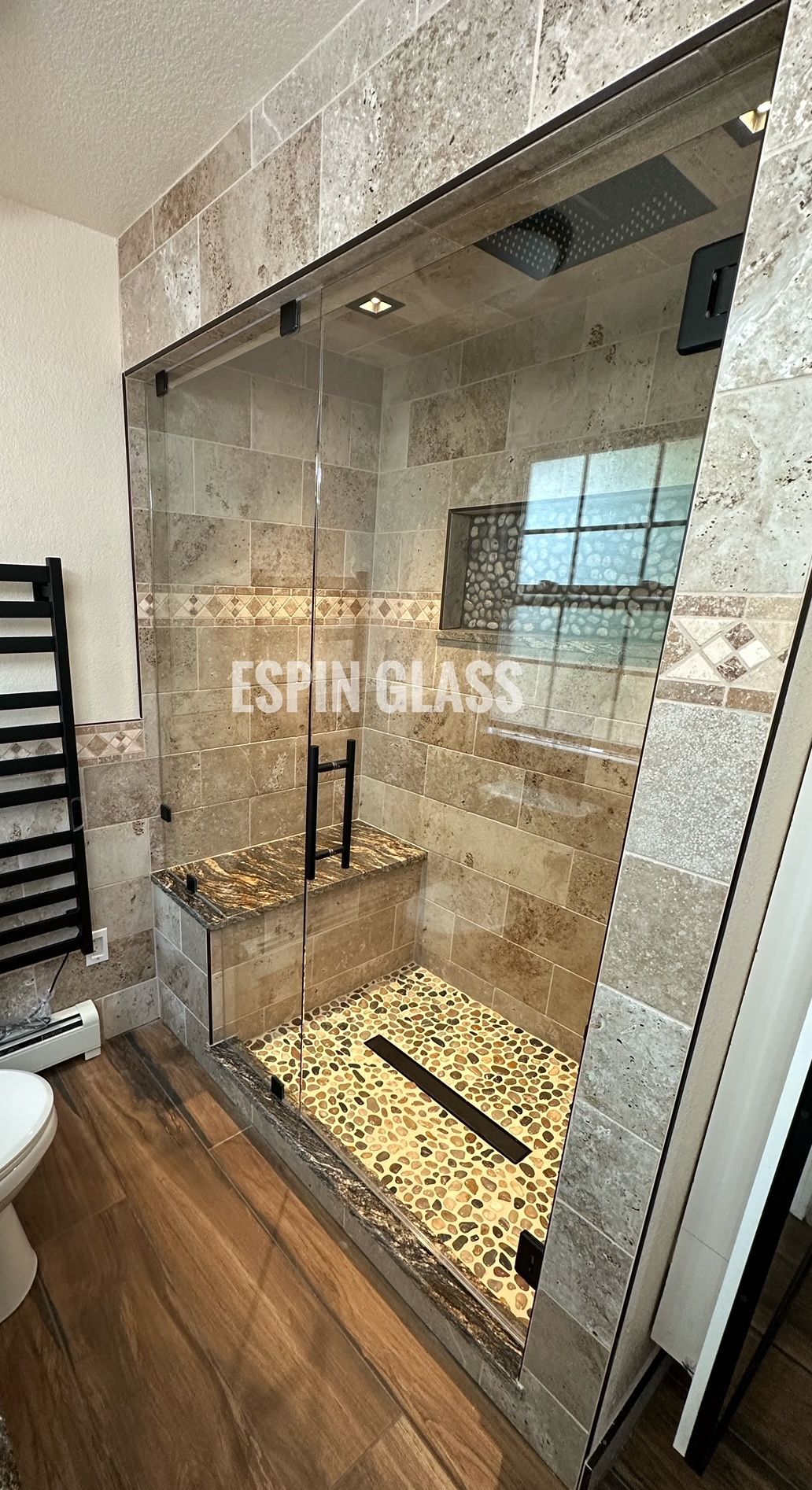 A luxurious bathroom with a glass shower, pebble floor, and stone walls.