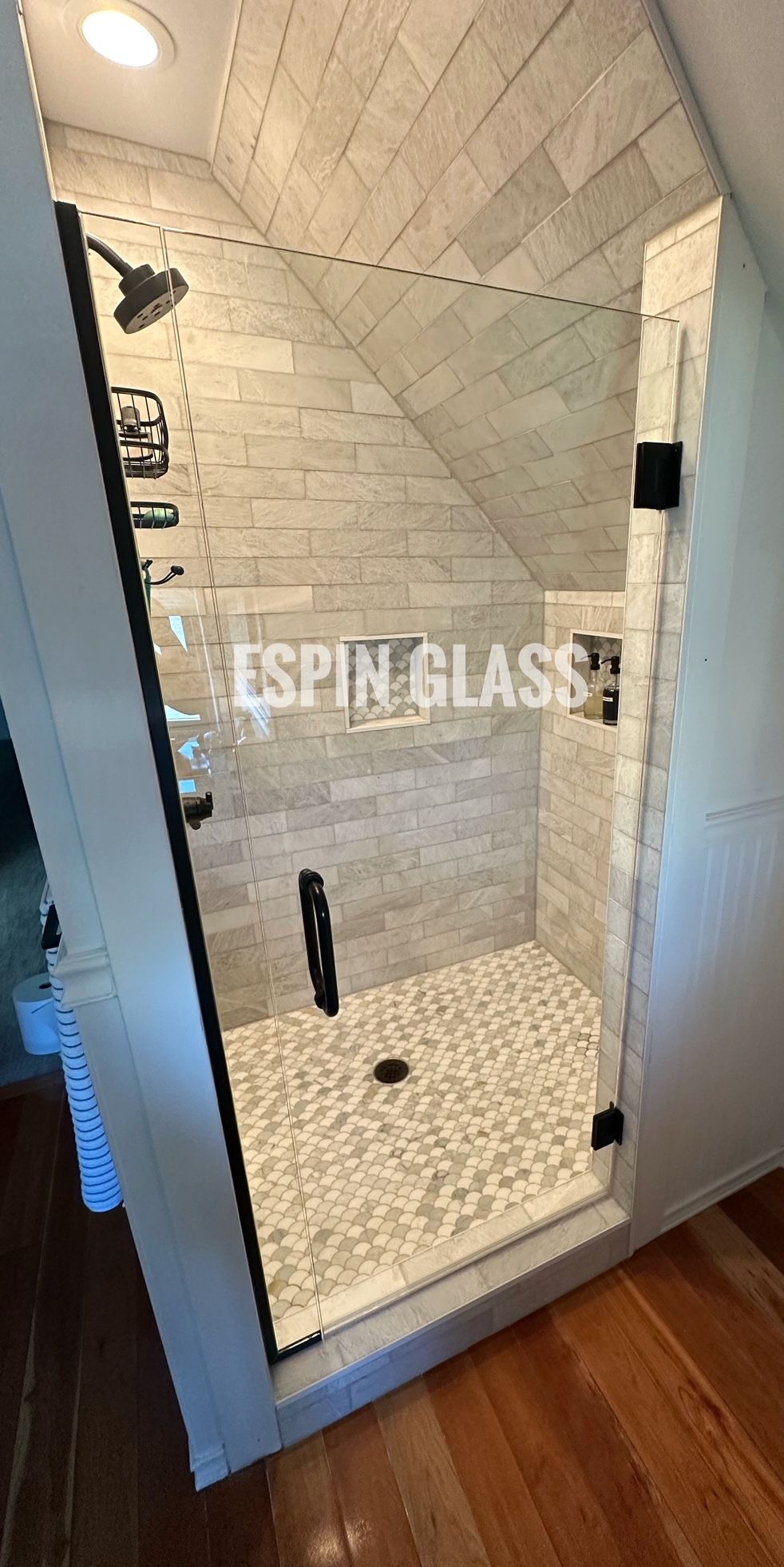 A modern shower with a pebble stone floor, glass door and brick style tiled walls.