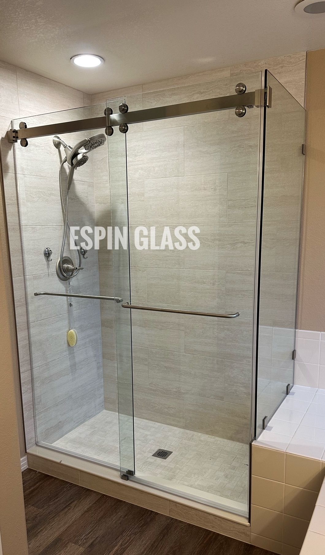 Glass shower enclosure with sliding door and stainless steel hardware.  Inside, a showerhead and controls are visible.