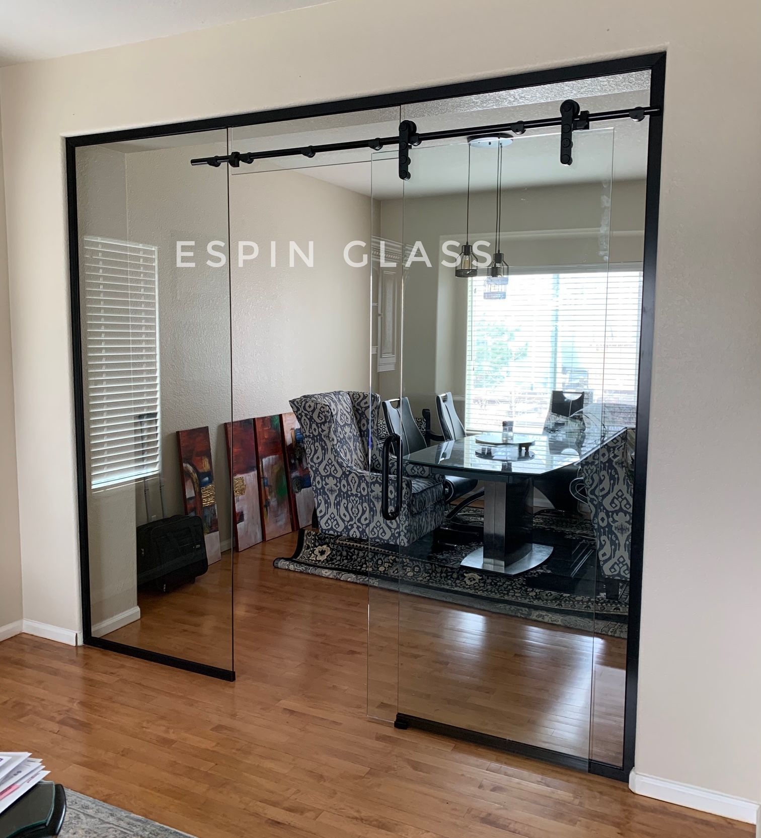 Glass sliding doors with black framing, open to a dining room.  Wood floors, a round table, and chairs are visible.
