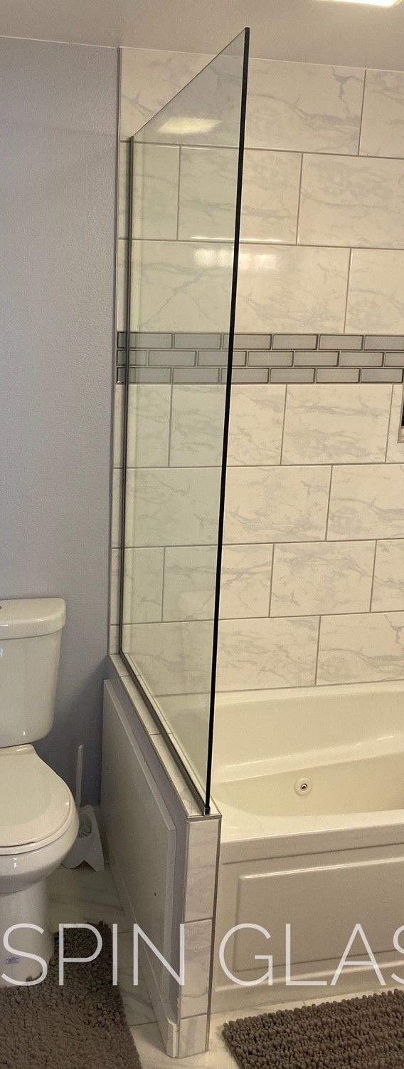 A shower with a glass partition next to a toilet in a bathroom. The walls are tiled with white tiles.