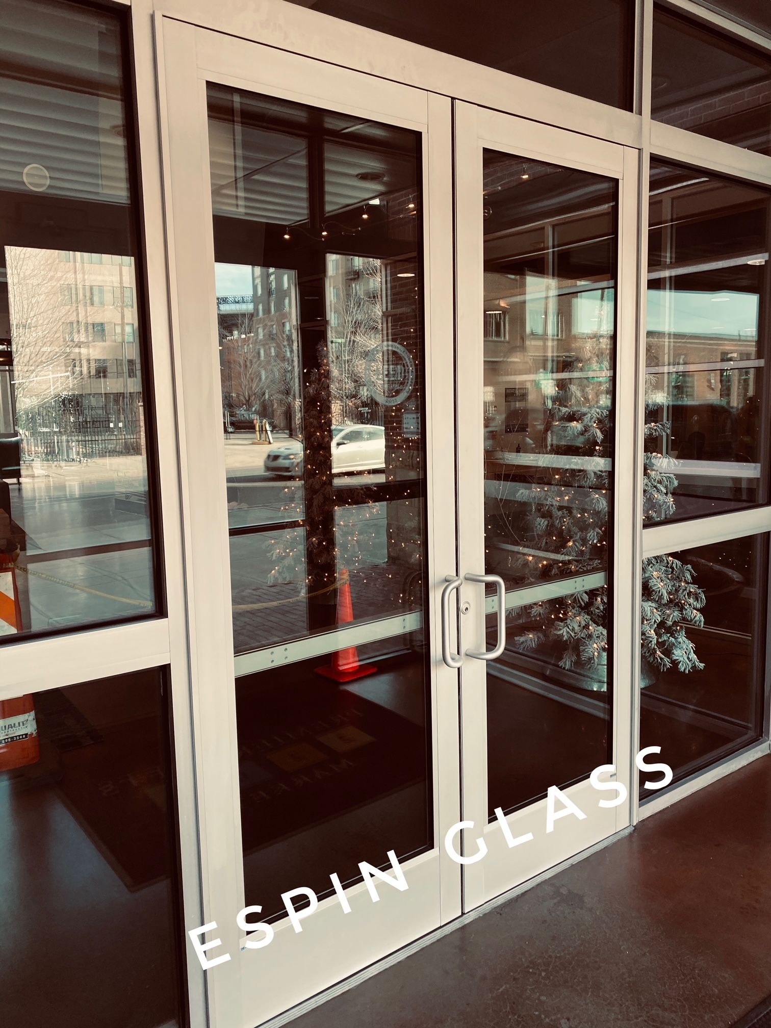 Exterior view of a building entrance with glass doors. White frames with stainless steel handles.