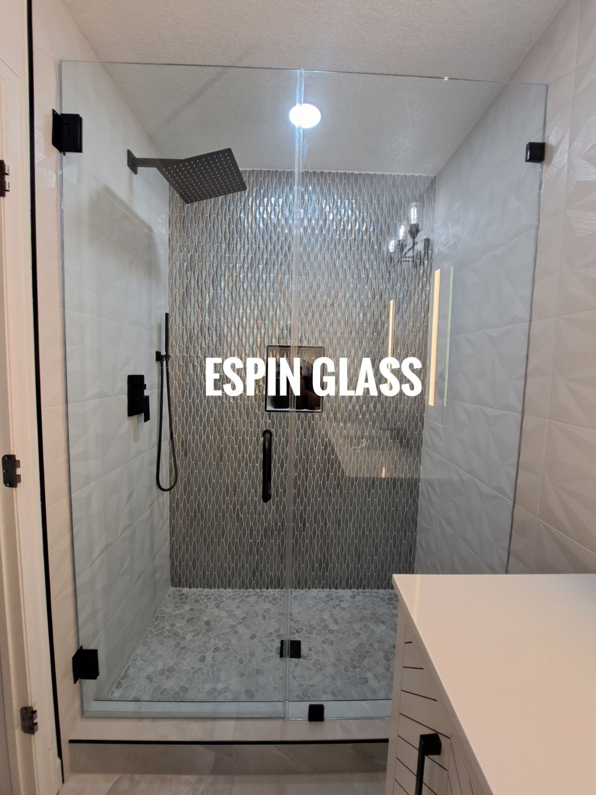 Glass shower enclosure with black hardware and mosaic tile accent wall.