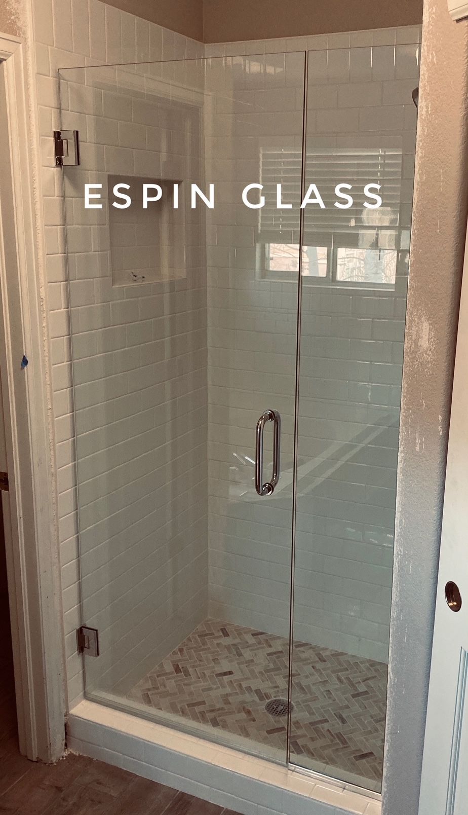 Frameless glass shower enclosure in a bathroom; white subway tile walls, glass door, and pebble-stone floor.