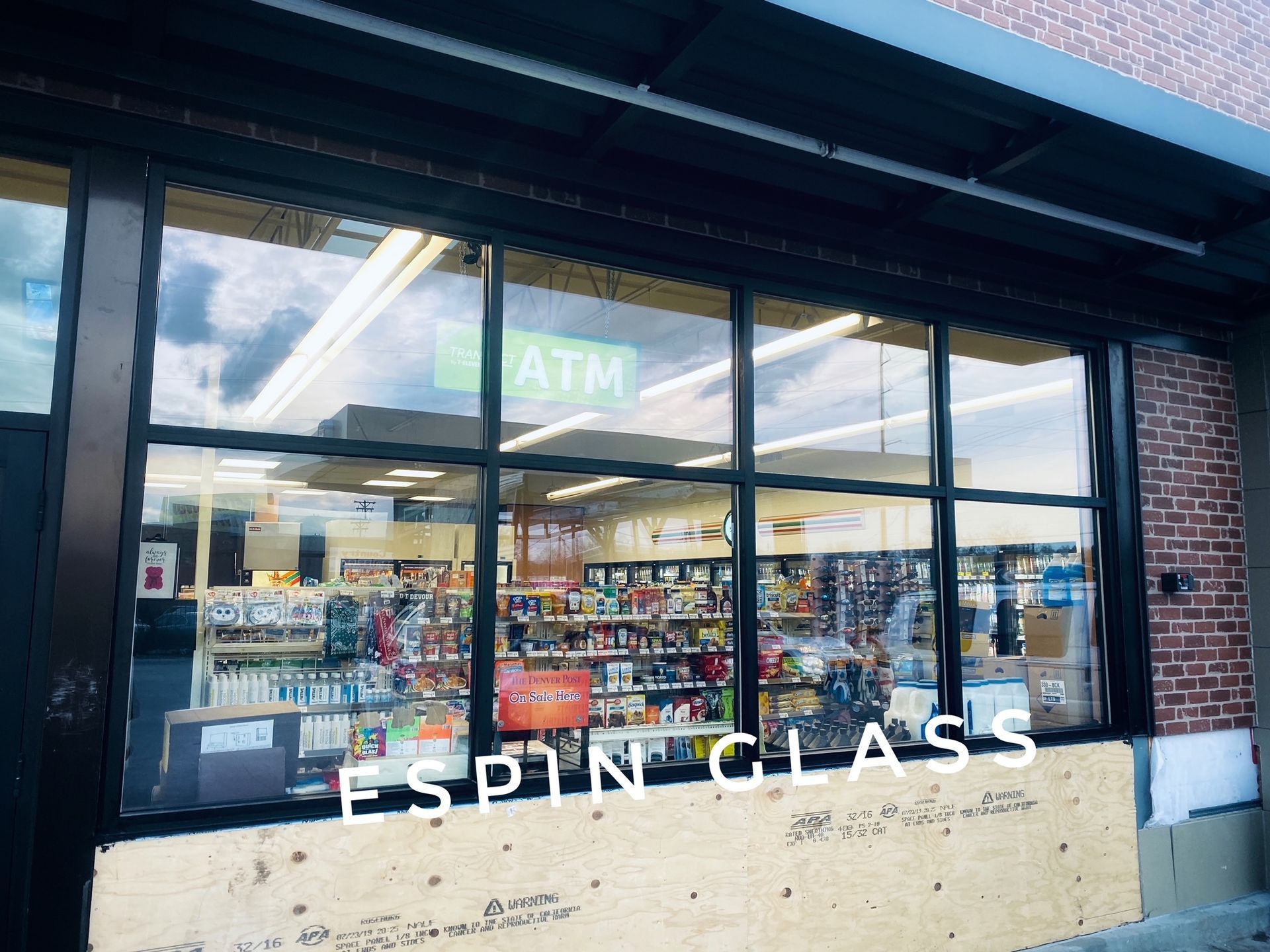 Convenience store exterior; window displays products. Green ATM sign. Storefront boarded up, with 