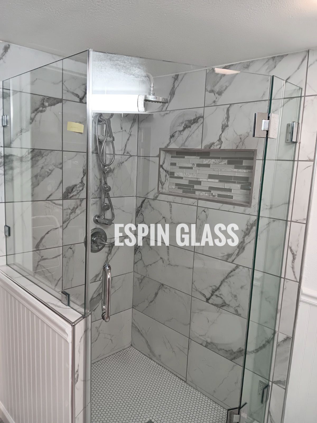 Glass shower enclosure with white marble tile and a mosaic niche.