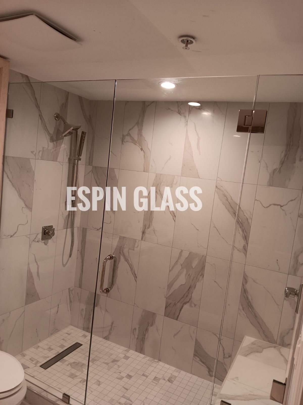 Glass shower enclosure with marble tile walls and floor.