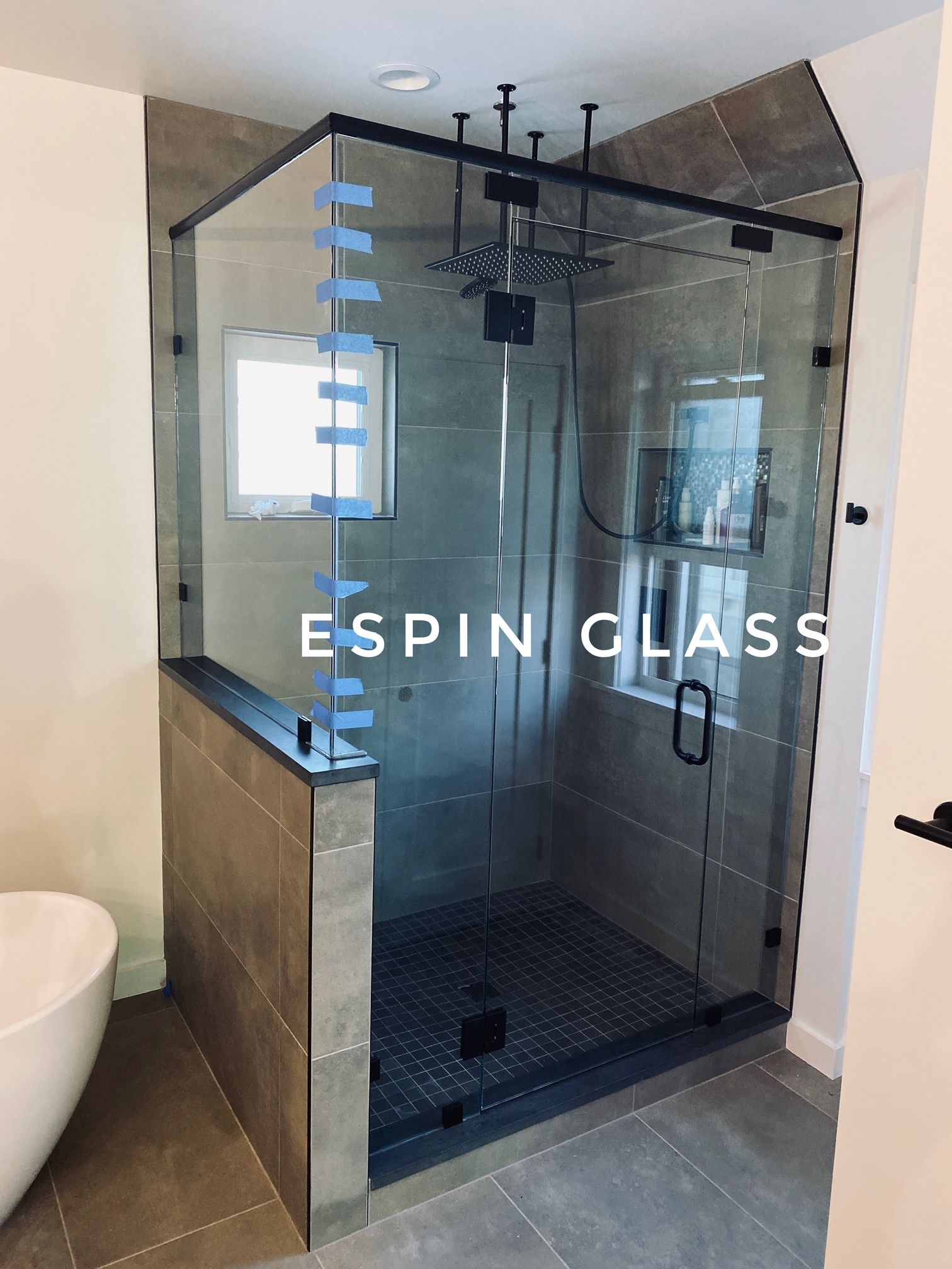 A modern shower enclosure with black framing, large glass panels, and a rain shower head.
