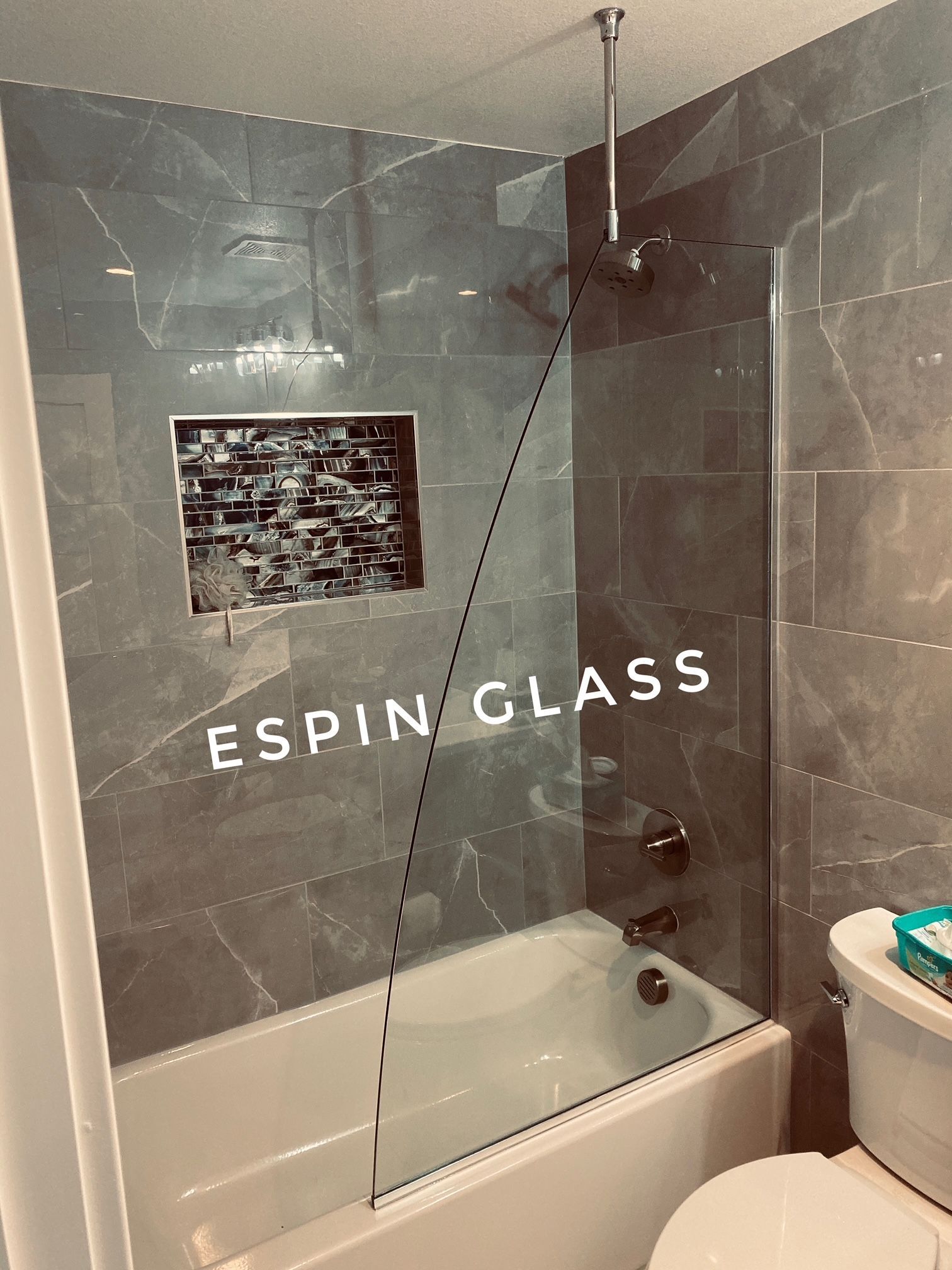 Bathroom with a gray tiled shower and glass door over a bathtub. A niche is visible with decorative tiles.