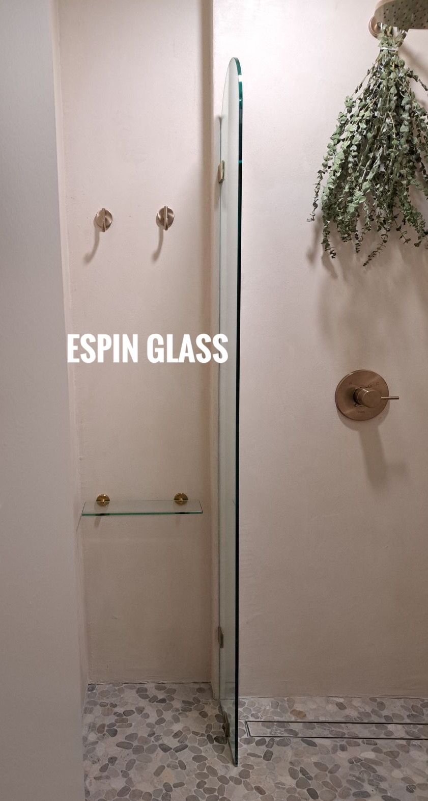 Bathroom with glass shower door, beige walls, small glass shelf, floral decoration, and decorative hardware.