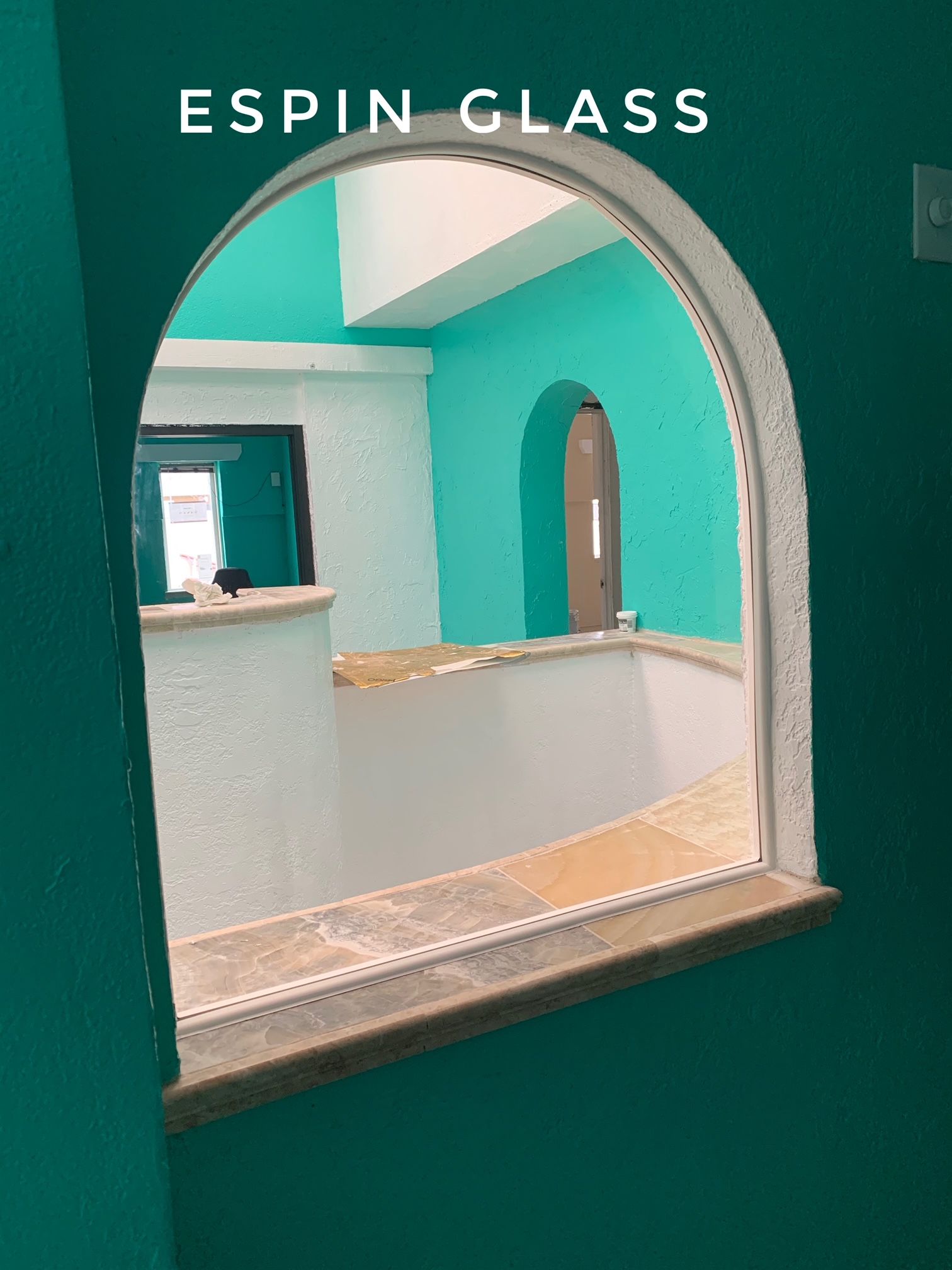 Arched window revealing an interior room with teal walls and white trim, labeled “ESPIN GLASS.”