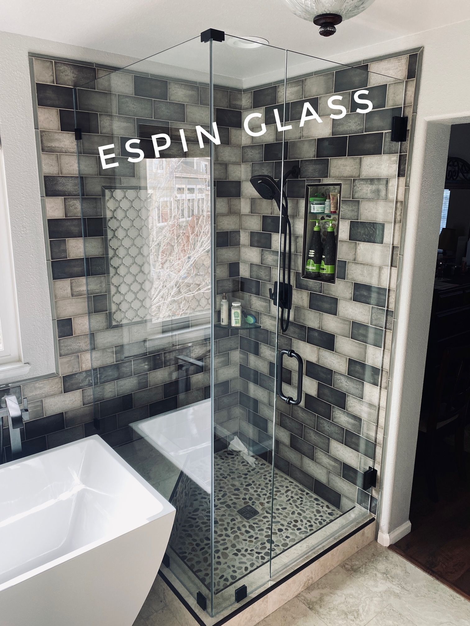 Glass shower enclosure with a stone-tiled wall and a white tub; the glass says 