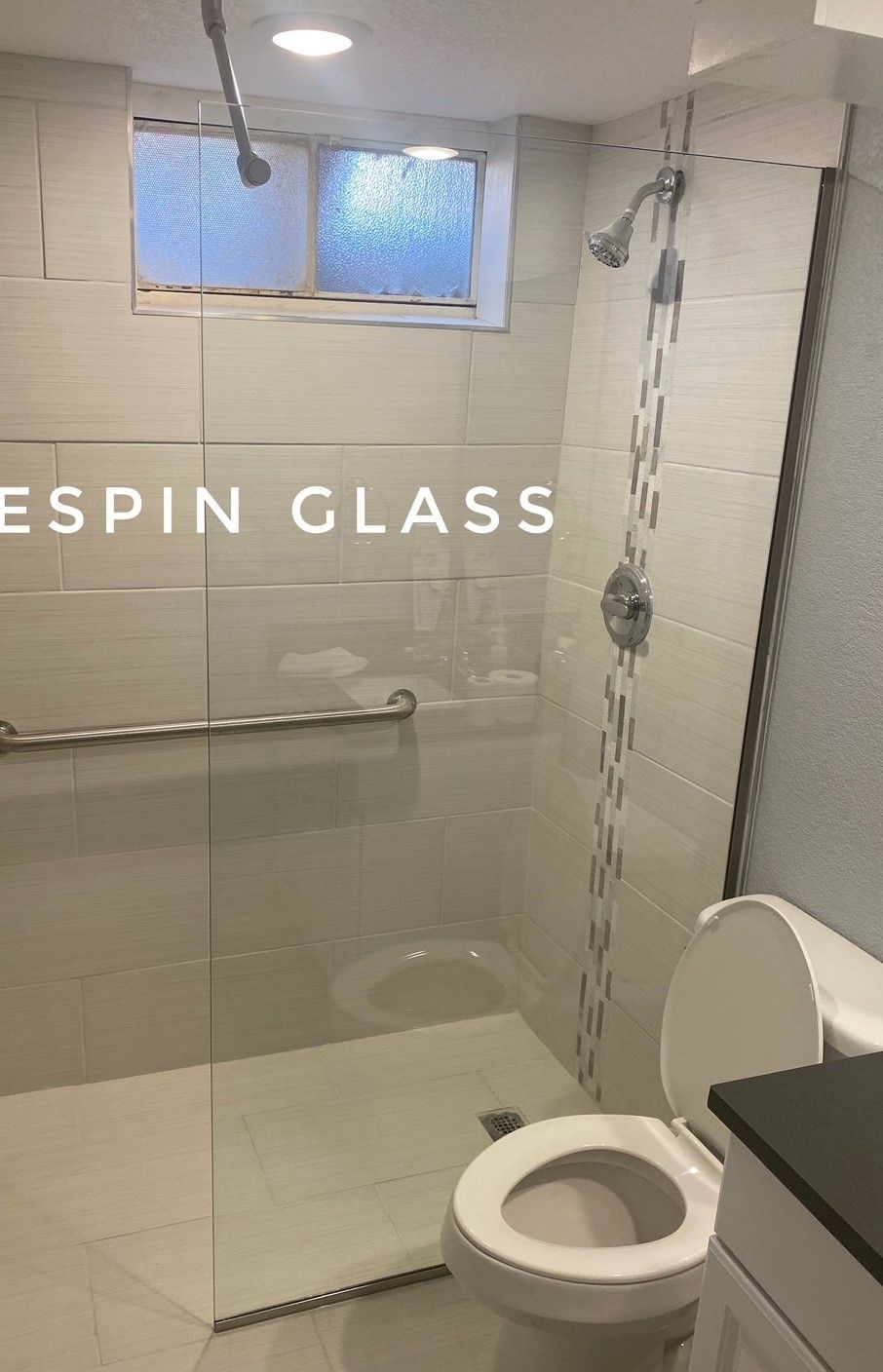Bathroom with a clear glass shower door, toilet, and white tiled walls.