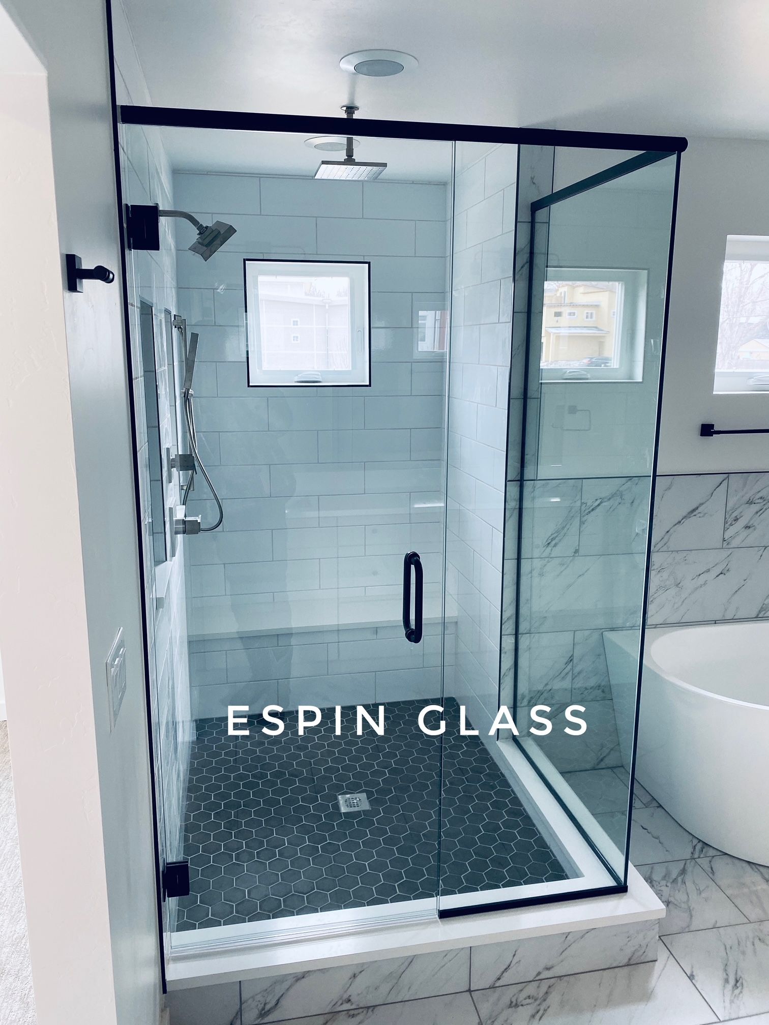 Black-framed glass shower enclosure with black hardware, a showerhead, and a dark stone floor in a bathroom.