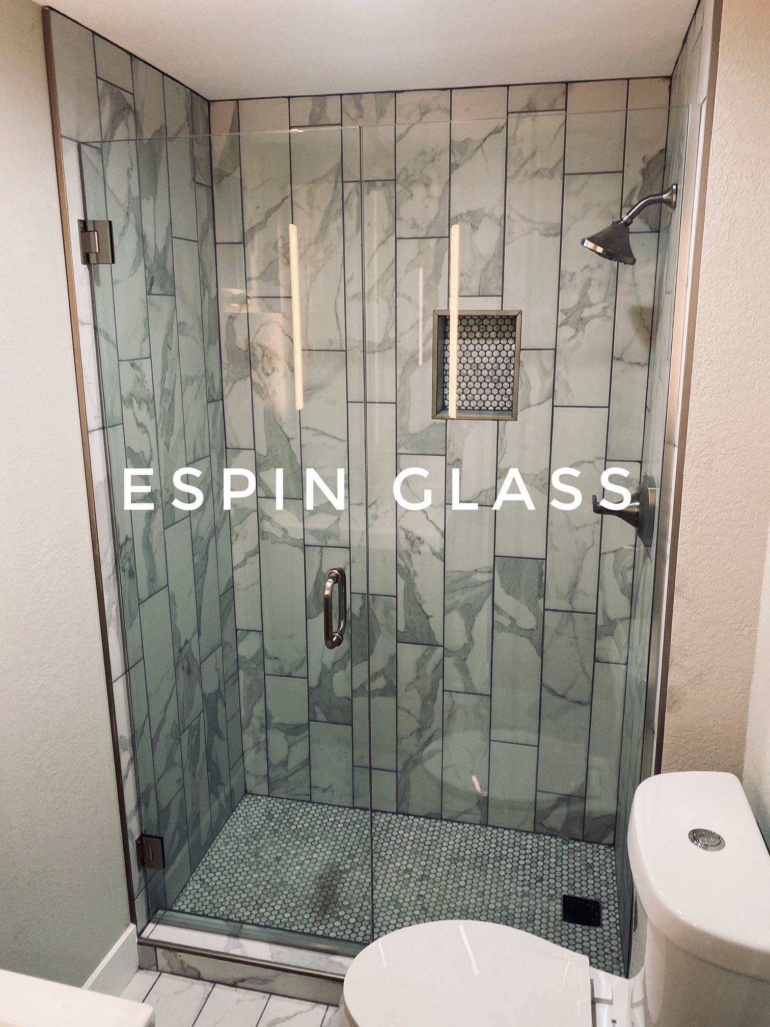 Glass shower with marble tile, stainless steel fixtures, and a white toilet.