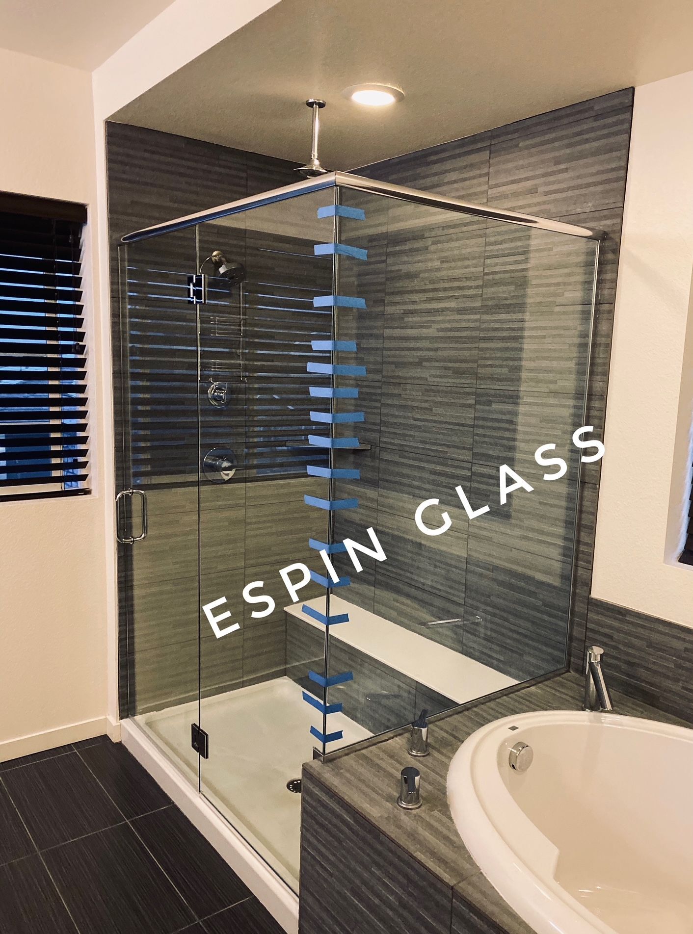 Modern glass shower enclosure with blue accents, gray tile, and a white bathtub in a bathroom.