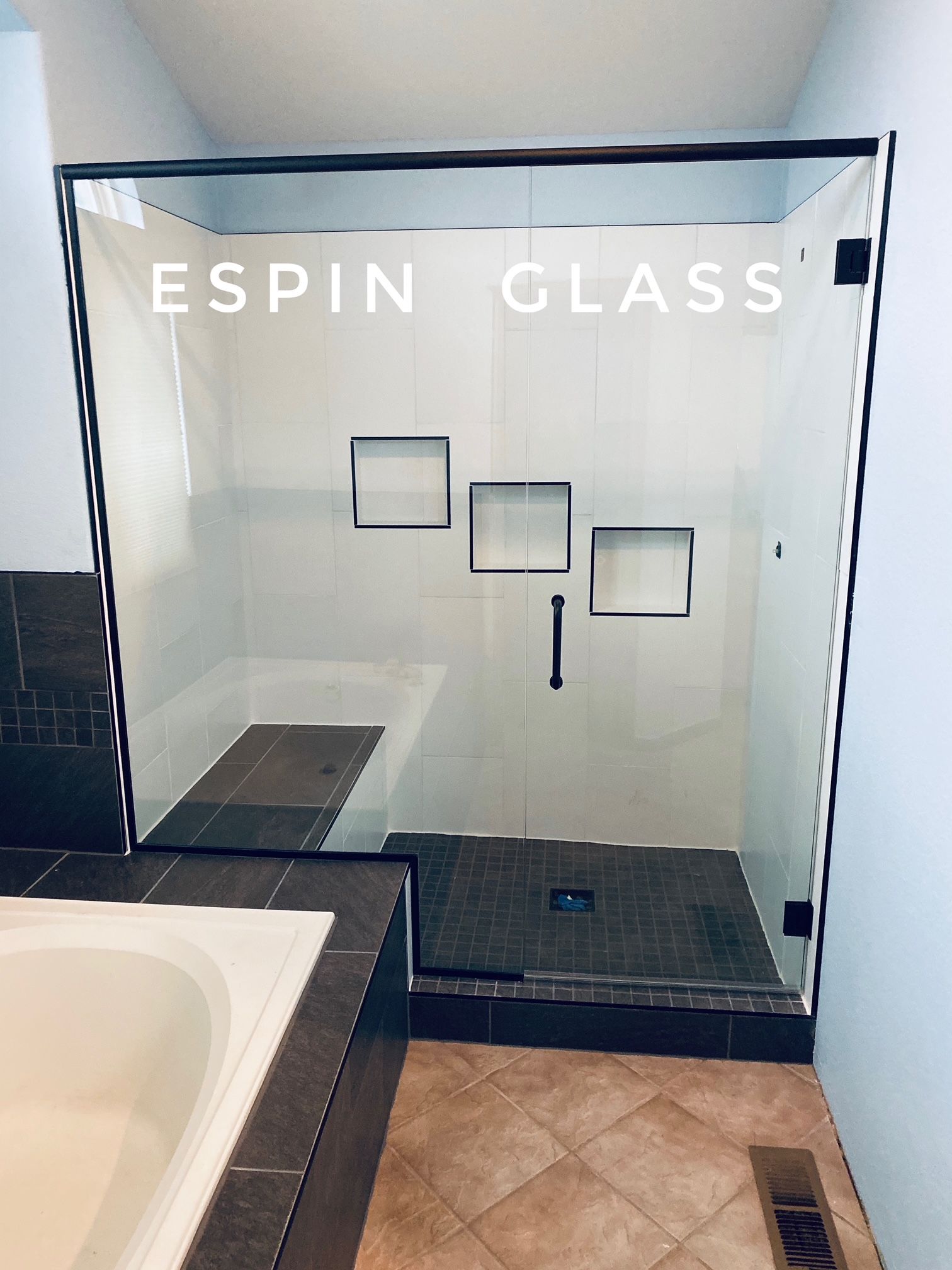 Glass shower with dark trim; brown tile floor, white walls, and a built-in bench.