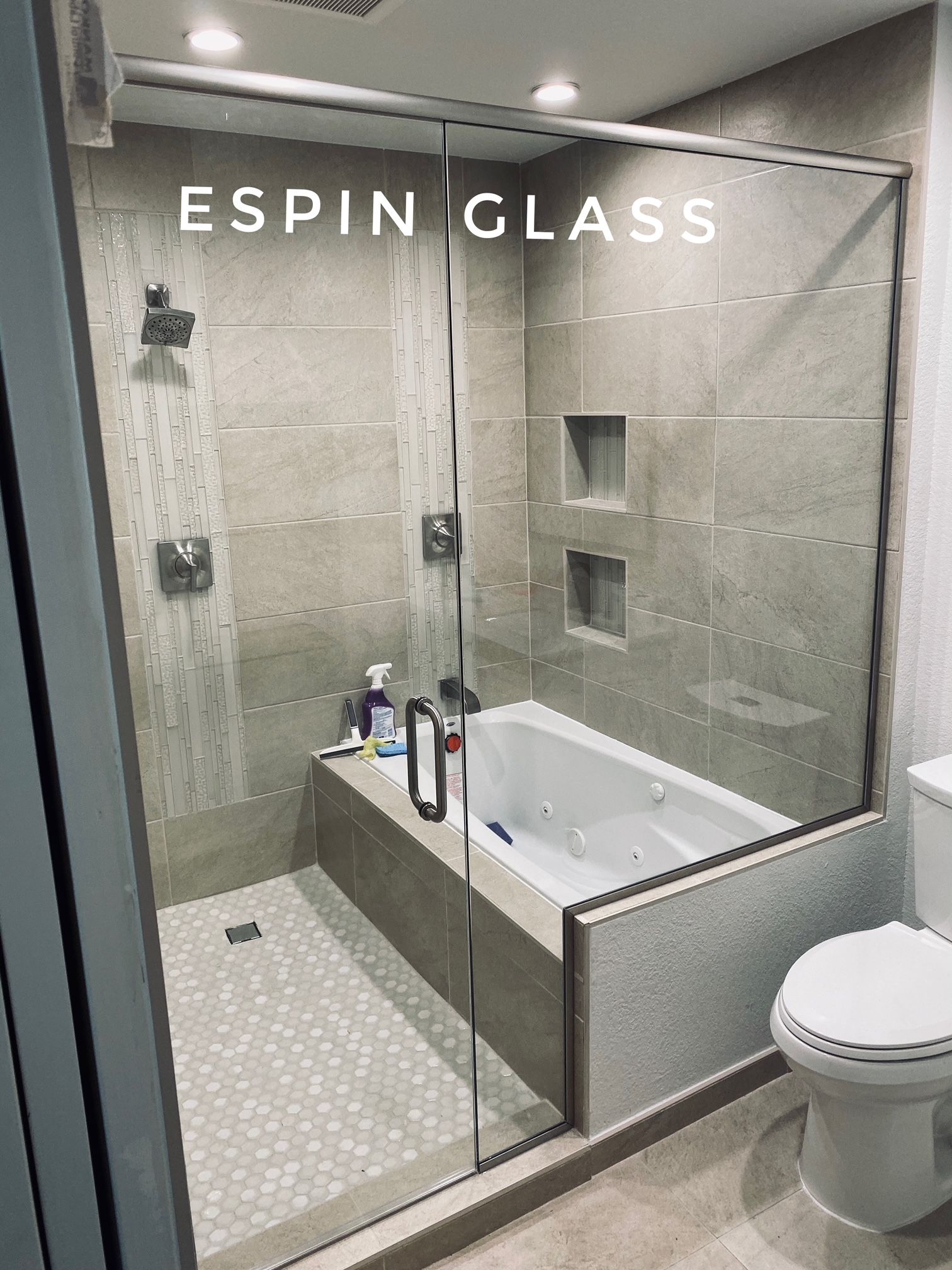Modern bathroom with glass shower door, bathtub, beige tile, and a toilet.