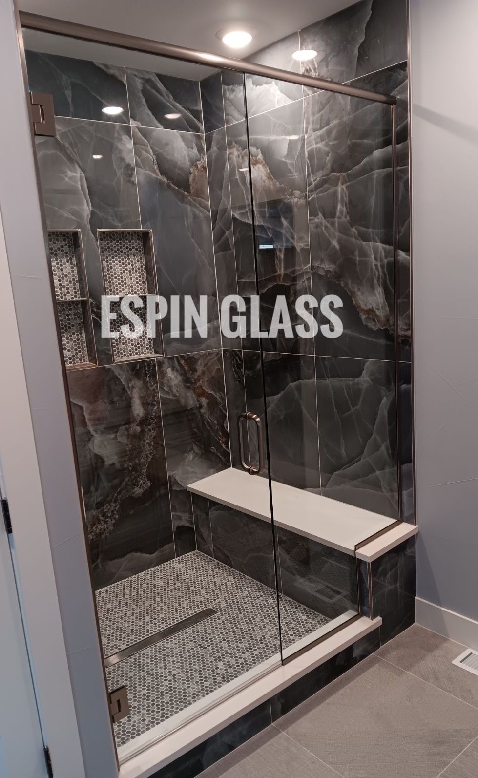 Modern bathroom with a glass shower door, dark marble tile walls, and a built-in bench.
