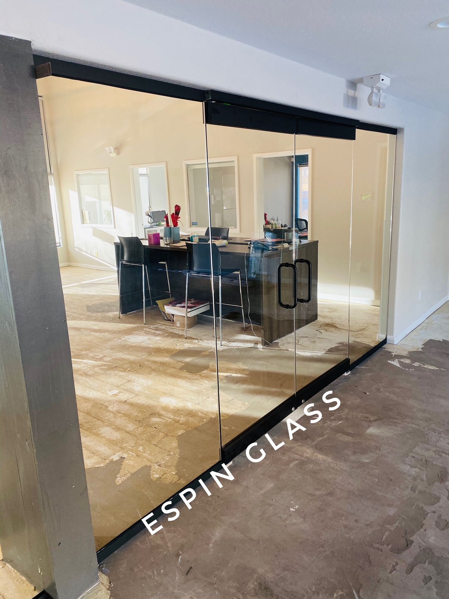 Glass sliding doors with black frame and handles leading into an office with a desk.