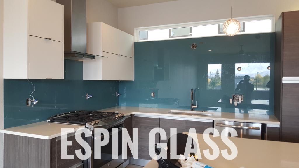 Modern kitchen with teal glass backsplash, white cabinets, and stainless steel appliances.