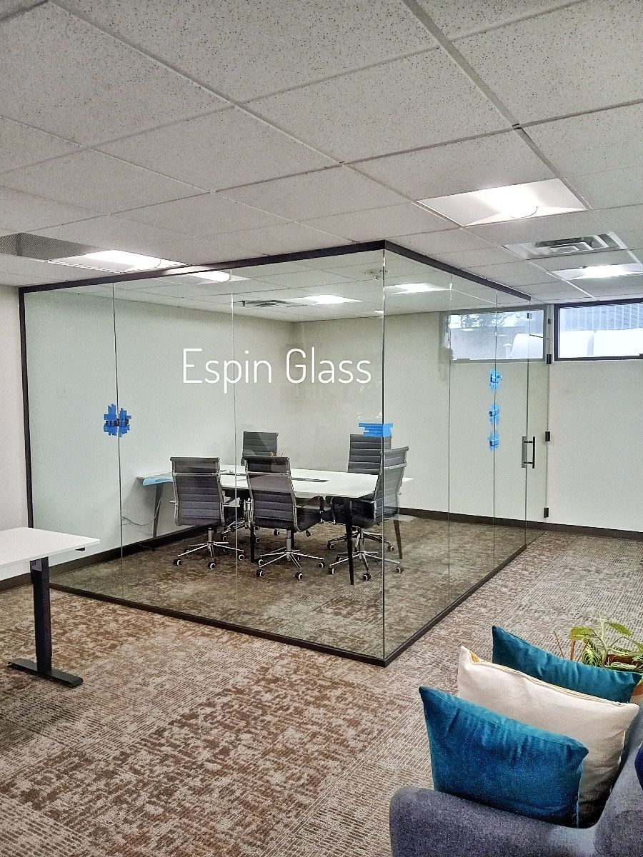 Meeting room enclosed by glass walls; office setting with table, chairs, and blue pillows.