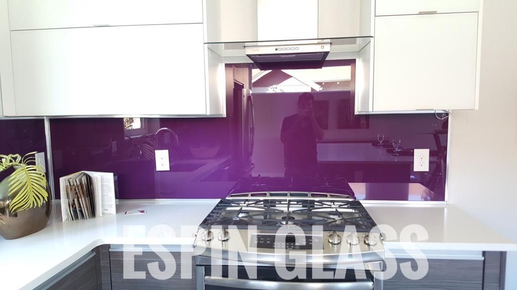 Purple glass backsplash in modern kitchen with white cabinets and gas stove.