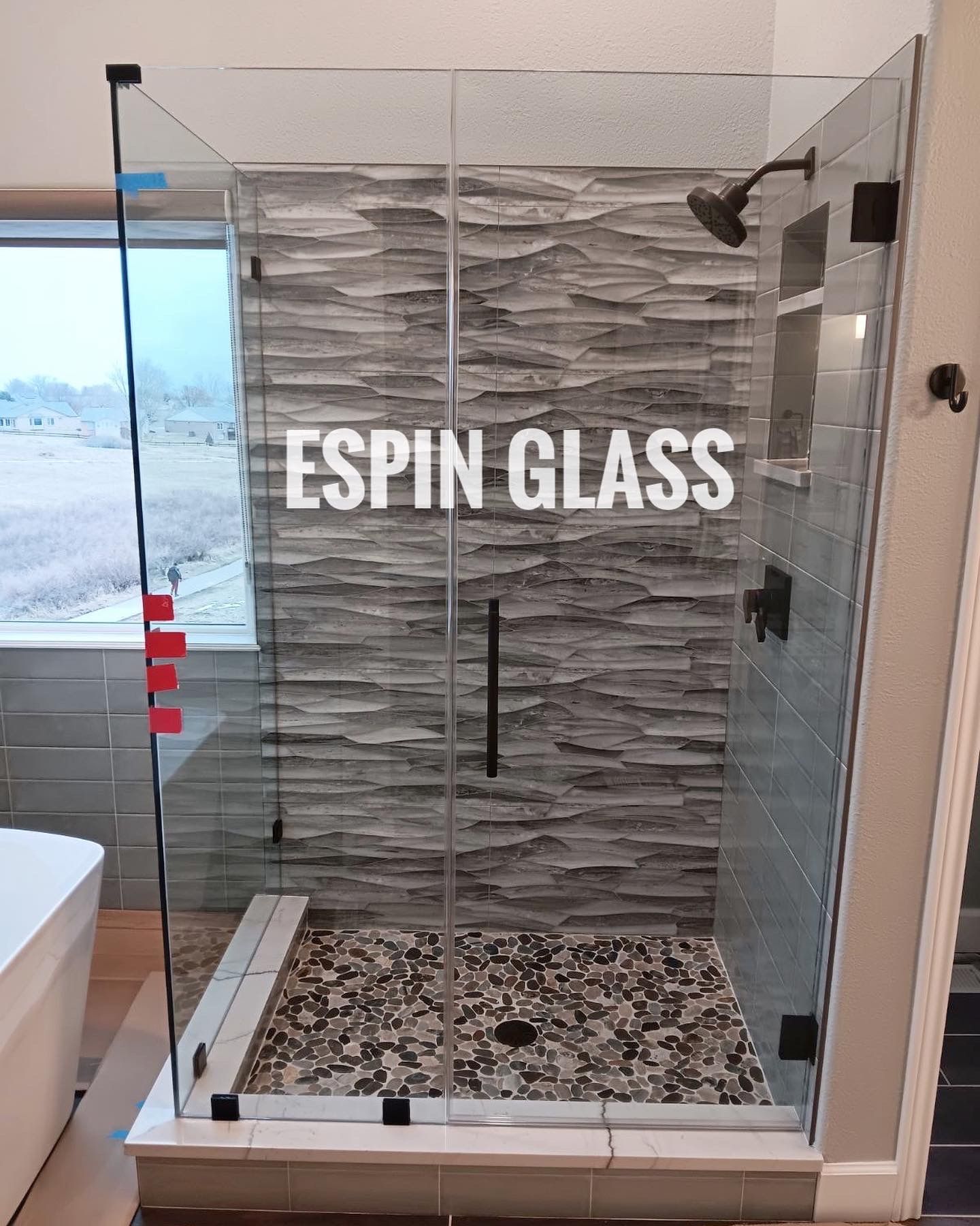 Frameless glass shower enclosure with black fixtures and pebble floor, set against gray textured tile wall.