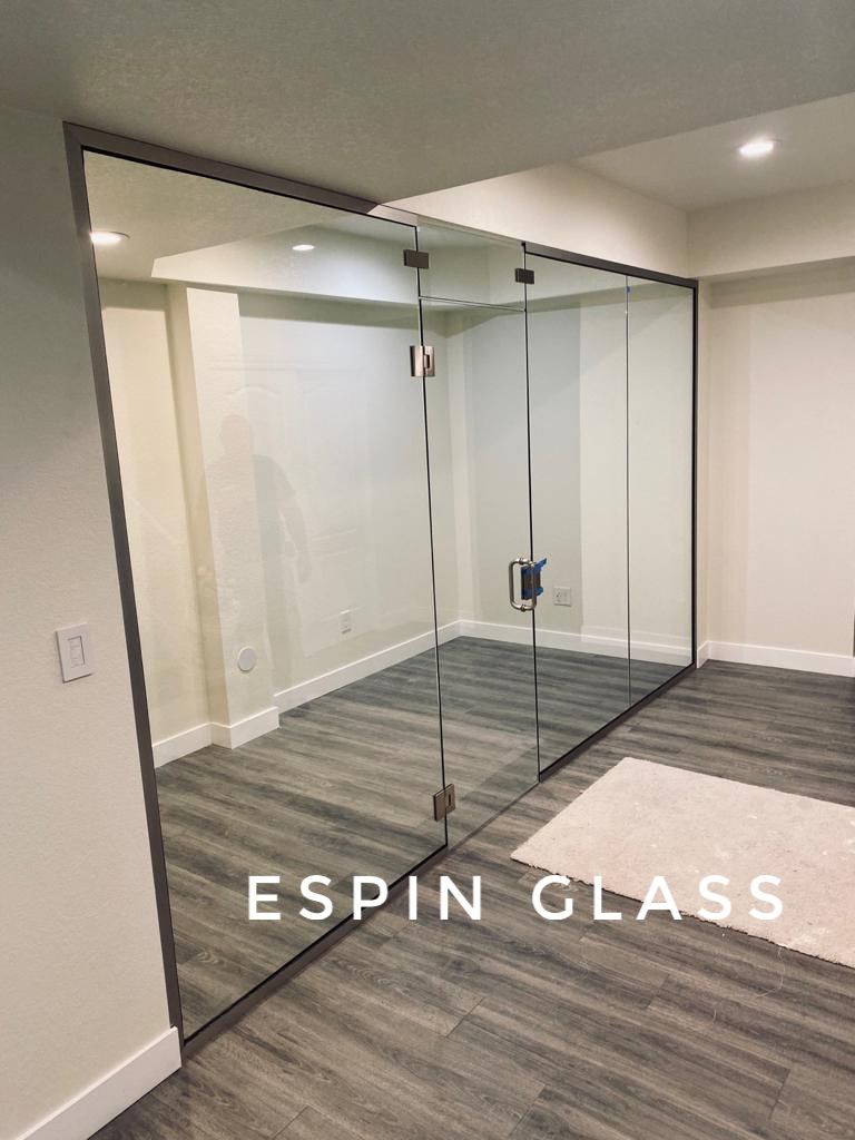 Glass-walled room. Clear panels with gray trim. Wooden floor. White walls.