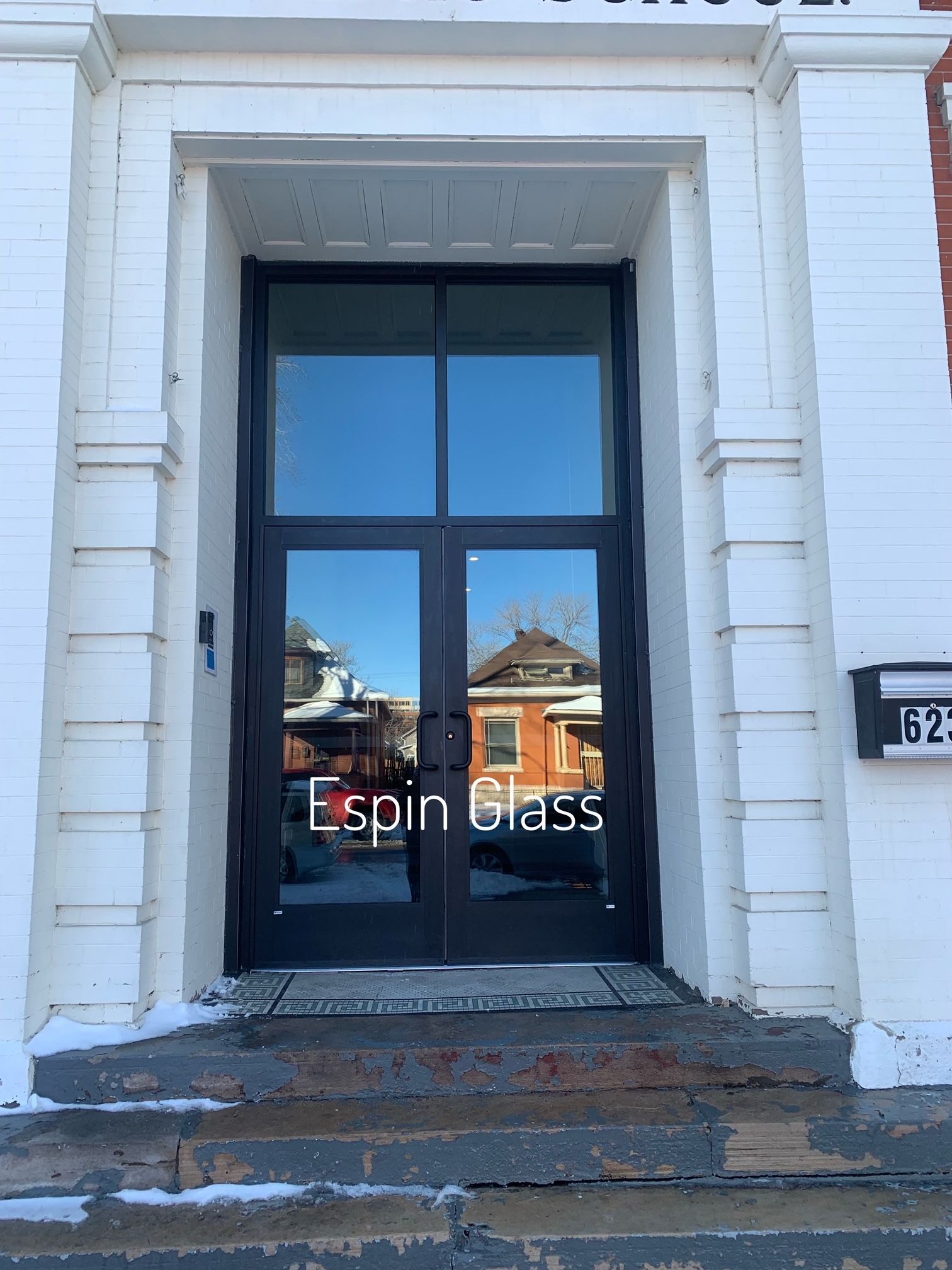 Black glass double doors with street reflections in white entryway, steps with snow.