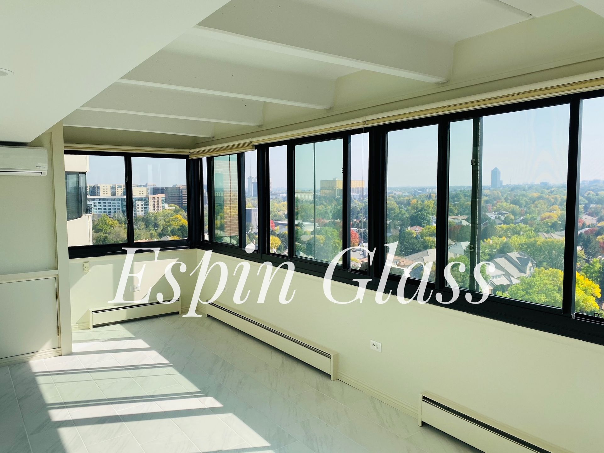 Bright room with floor-to-ceiling windows, black frames, looking out to a city view. White walls and ceiling.