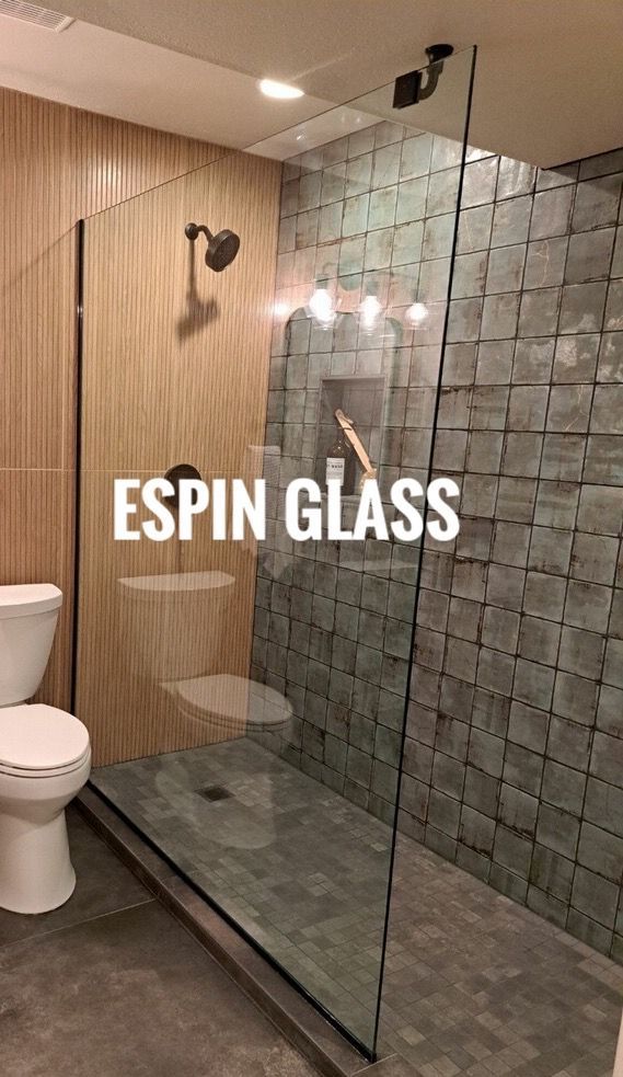 Modern bathroom with frameless glass shower. Textured stone and wood-look tile. Black fixtures, toilet on left.