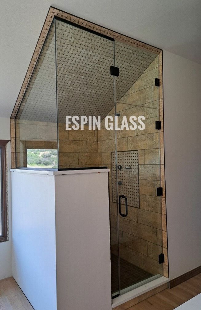 Glass shower enclosure with black hardware, tan tile, and white surrounding wall.
