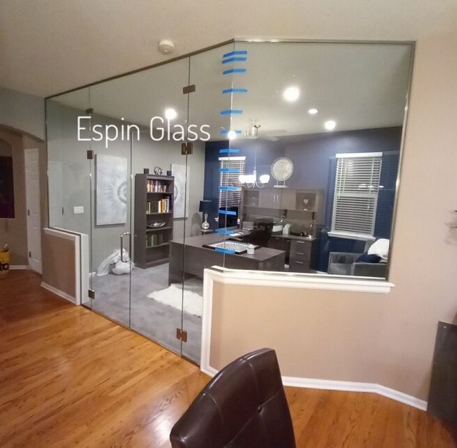 Glass-walled home office with desk, bookshelf, and chair visible through the clear glass, a modern design.