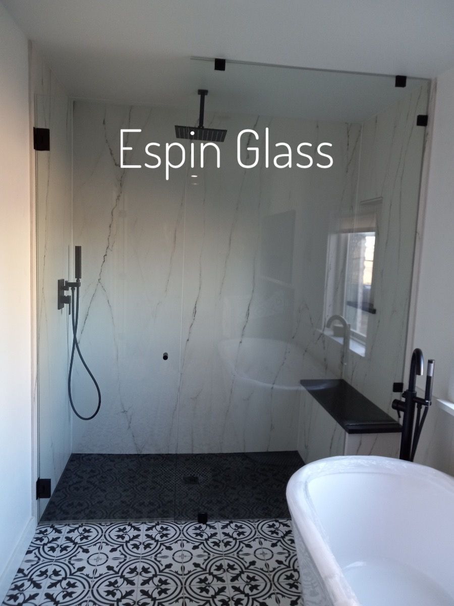 Modern bathroom with marble shower and patterned floor. Black fixtures, glass enclosure, and a white tub.