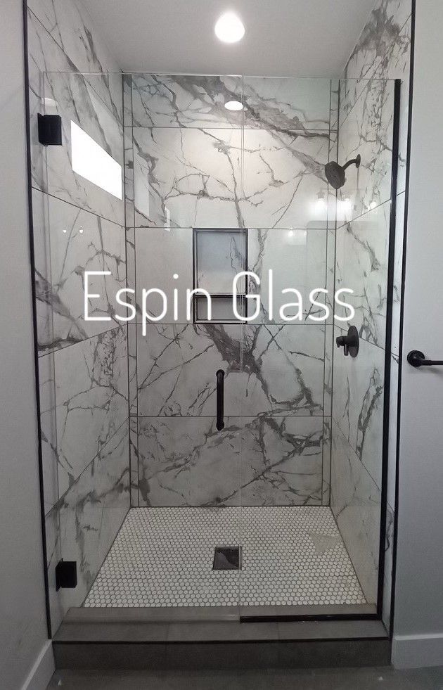 Glass shower enclosure with marble-patterned walls and a mosaic tile floor. Black fixtures.