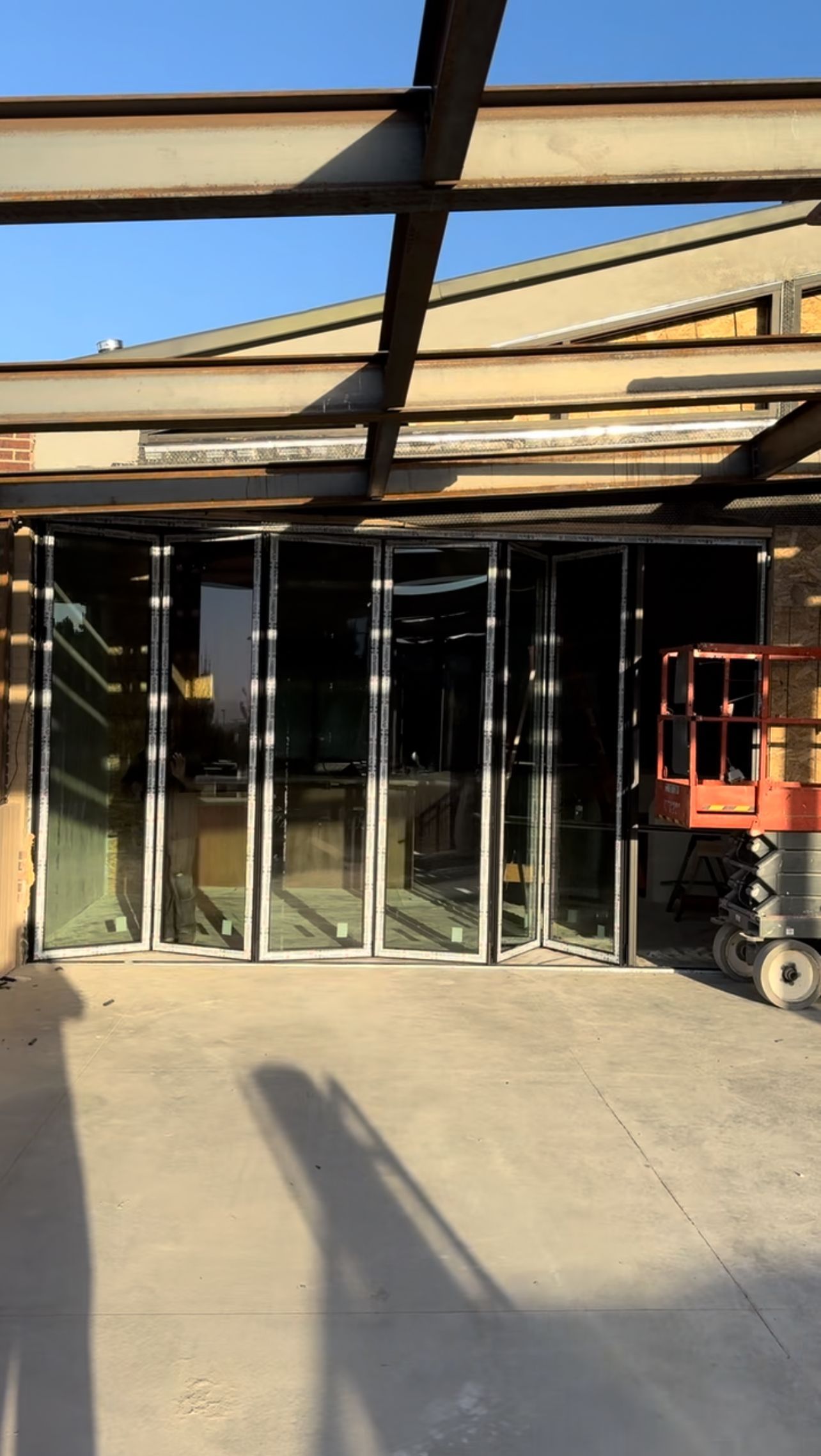 Exterior view of a building under construction with large glass folding doors and metal support beams.