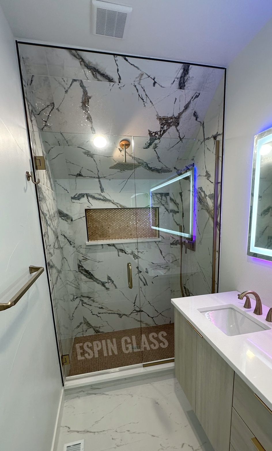 Marble-look shower with glass doors and gold fixtures in a modern bathroom.