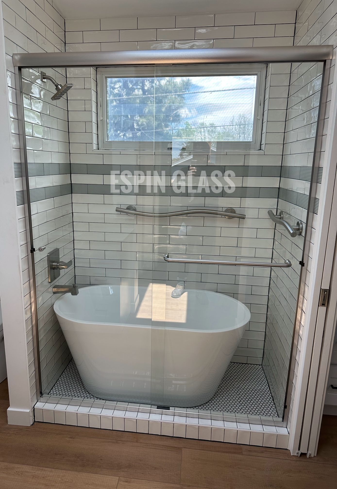 Bathroom with white soaking tub, glass shower door, white and gray tile, and window.