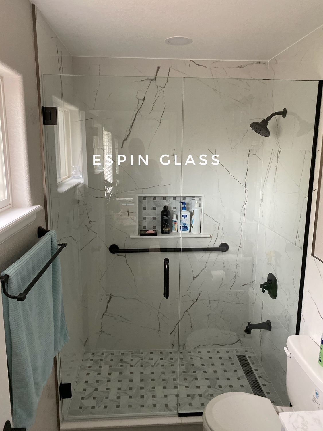 Modern bathroom with glass shower doors, white marble tile, black fixtures.