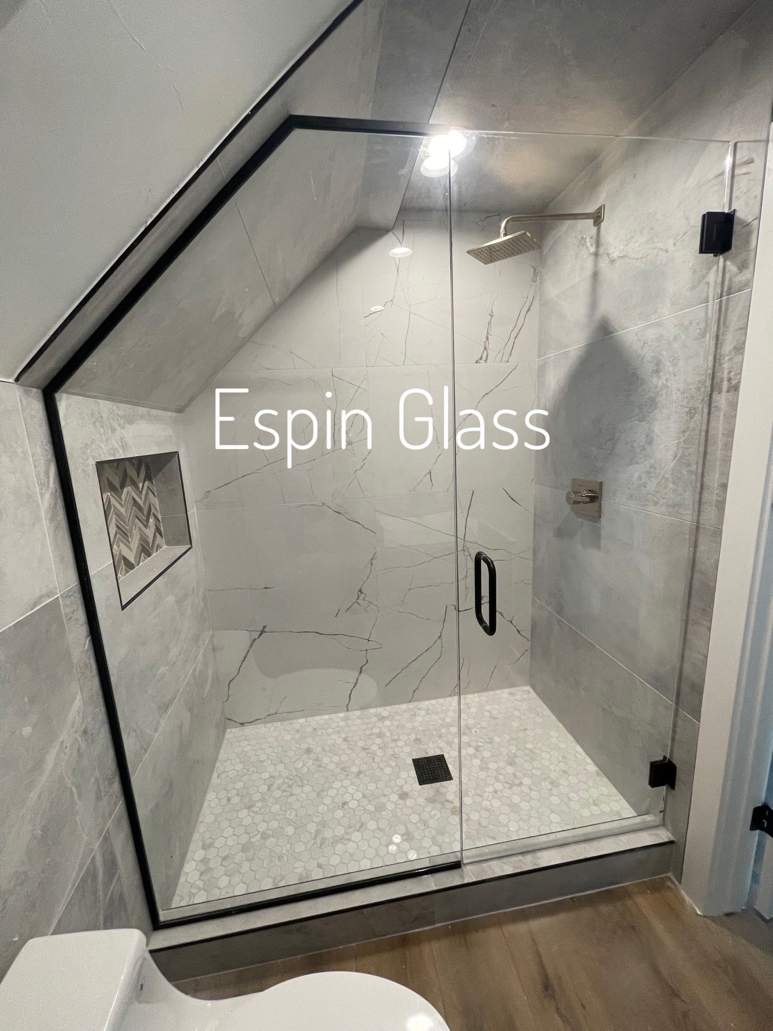 Modern glass shower with gray tiled walls, angled ceiling, and black door frame and hardware.