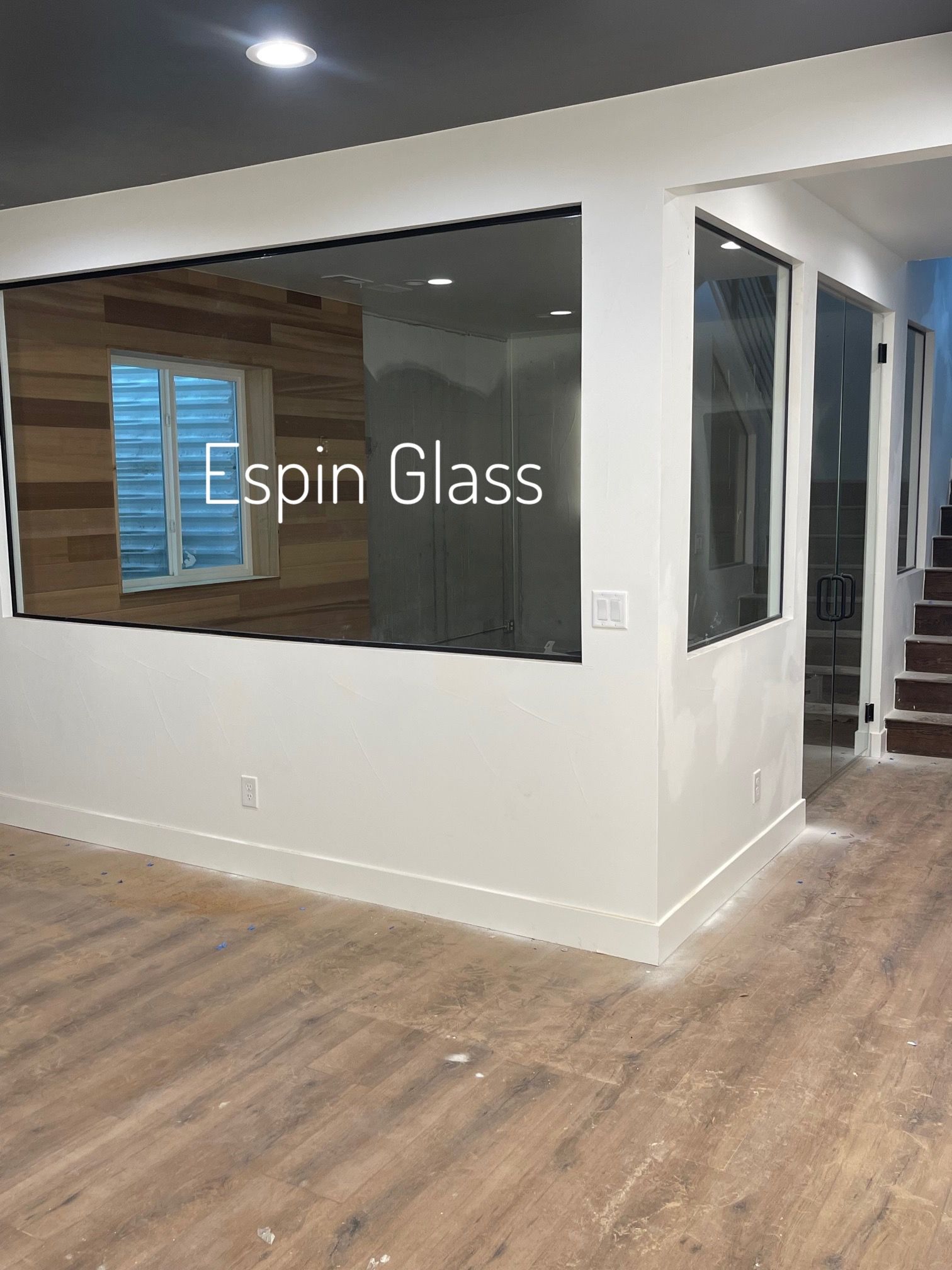 Interior view of a room with a large glass window. The wall is white with brown wood paneling and the floor is light brown.