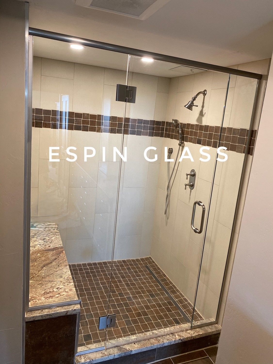 Shower with glass door, brown and beige tile, dark trim, granite bench.
