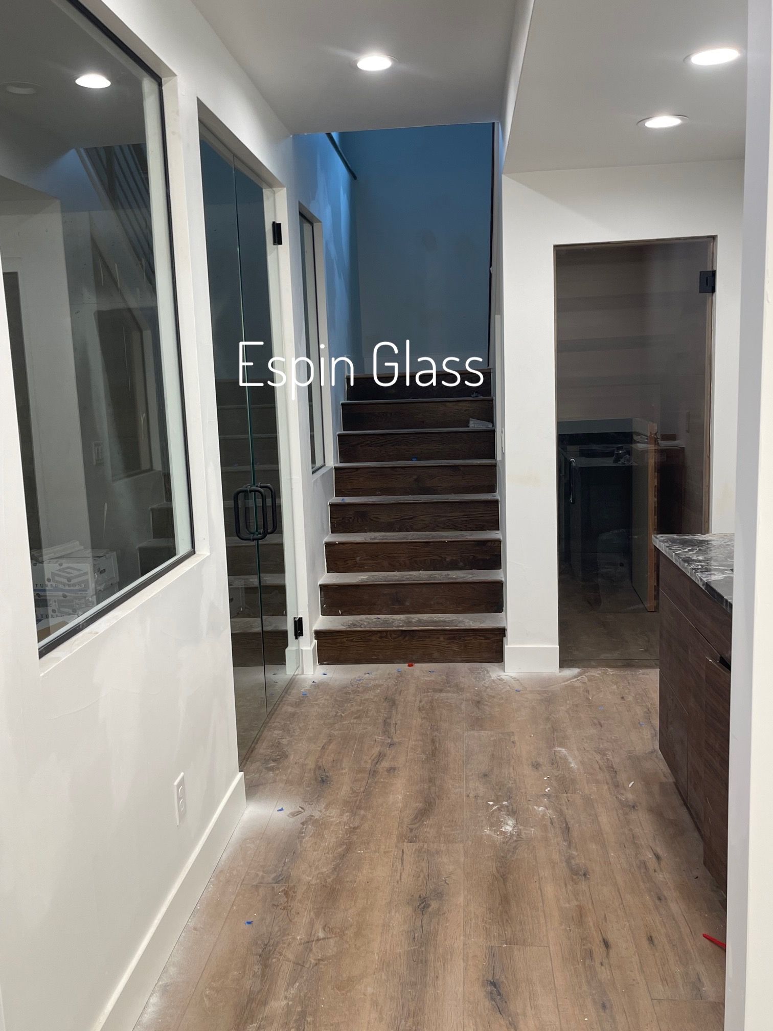 Hallway with glass doors and stairs. Wooden flooring, white walls. 