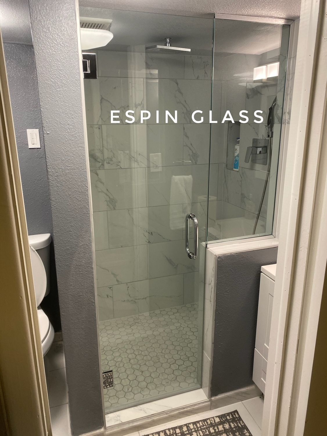Glass shower enclosure with white and gray tile, small bathroom. 