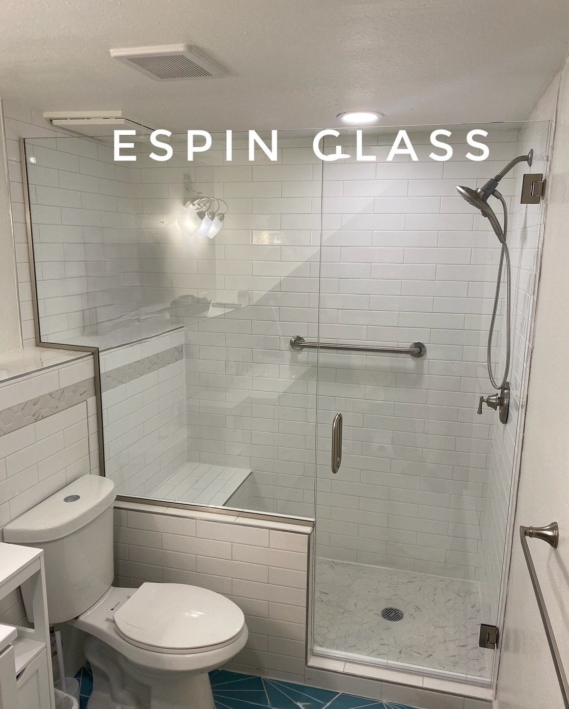 Shower enclosure with clear glass doors, white tile, and a toilet in a bathroom.