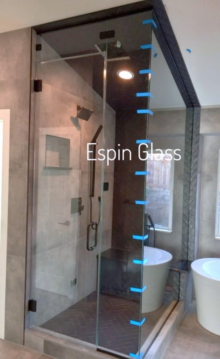 Modern glass shower enclosure with black hardware in a bathroom with gray walls, a bench, and a freestanding tub.